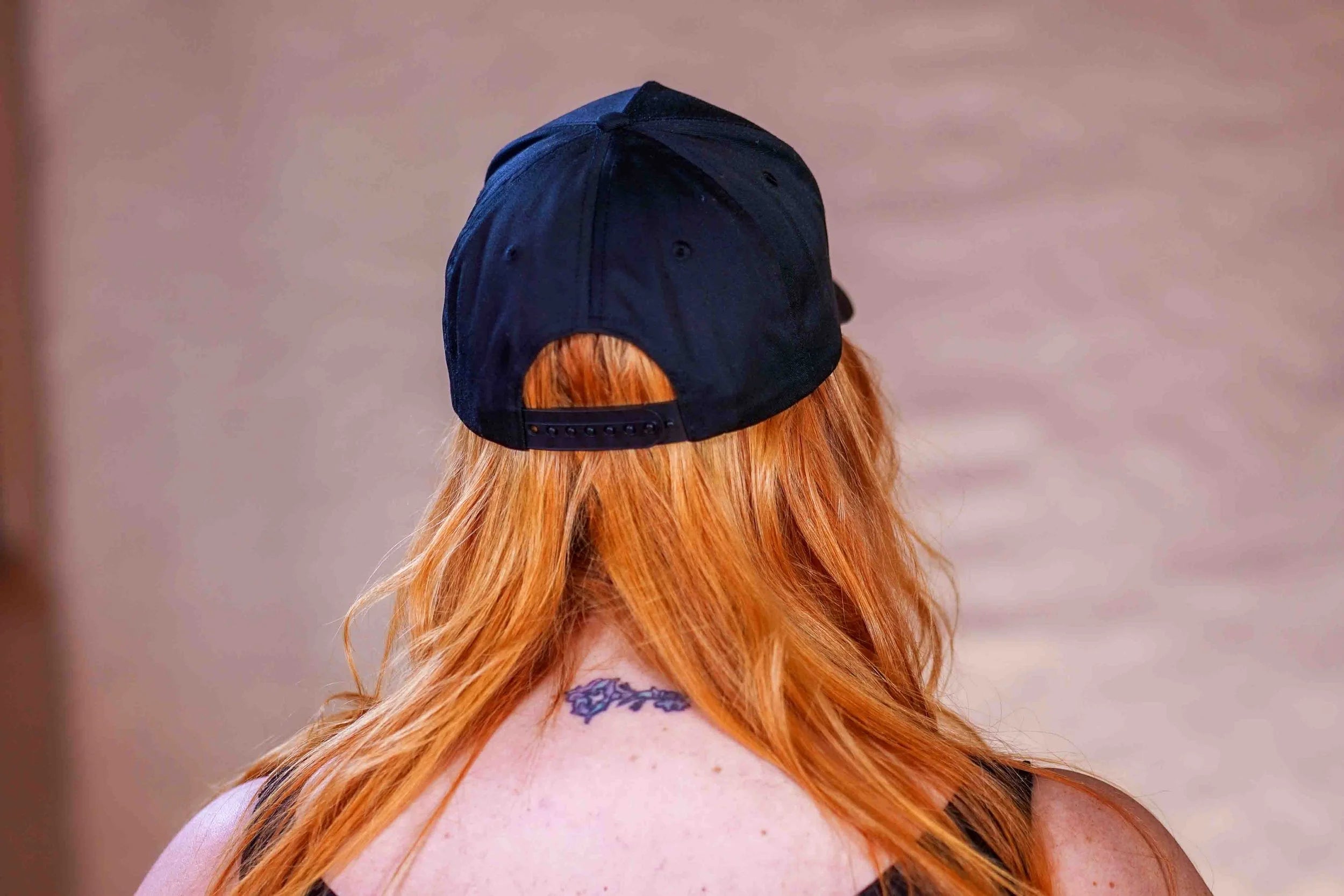 Person with red hair wearing a black cap, back view
