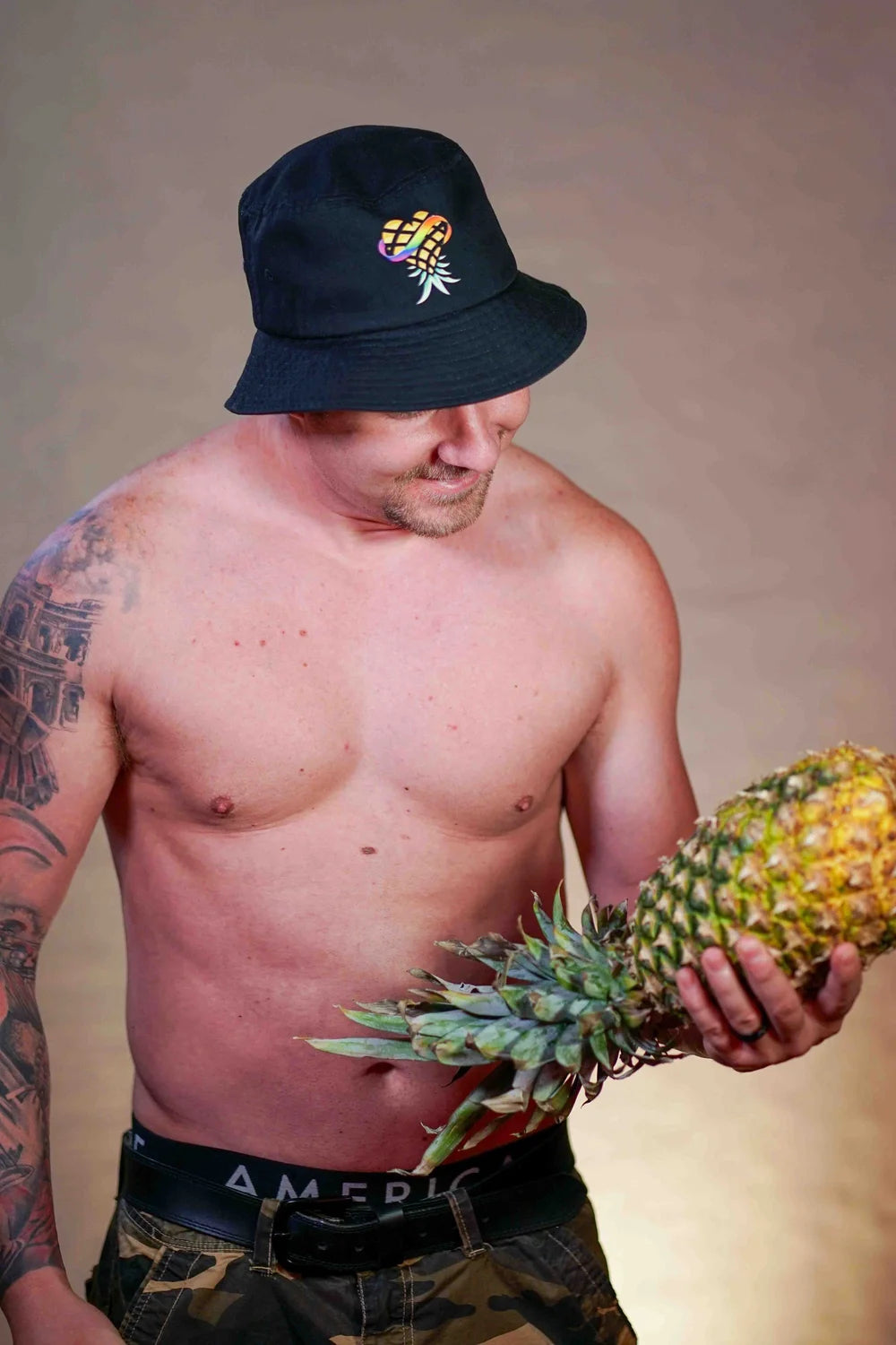 Man wearing a black bucket hat and holding a pineapple against a neutral background