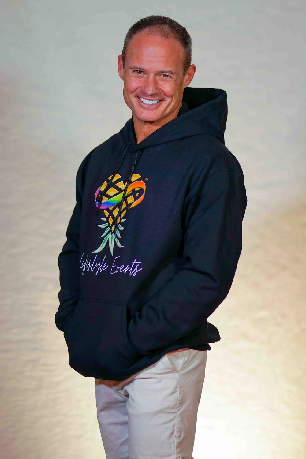 Man wearing a black hoodie Polyamerous Upsidedown Pineapple Logo Hoodie with a colorful graphic and text on a plain background
