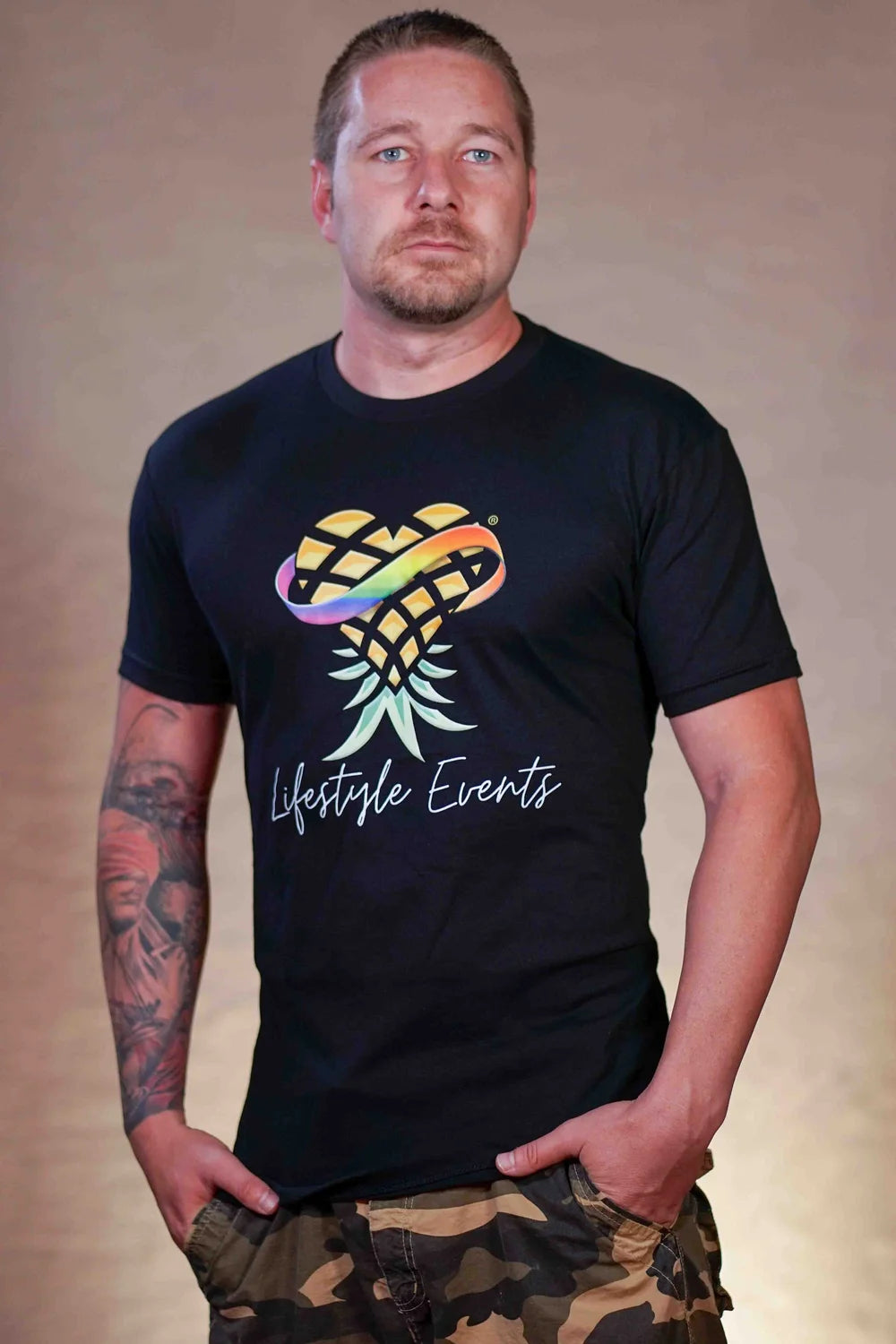 Man wearing a black t-shirt with a colorful logo and text, standing against a beige background