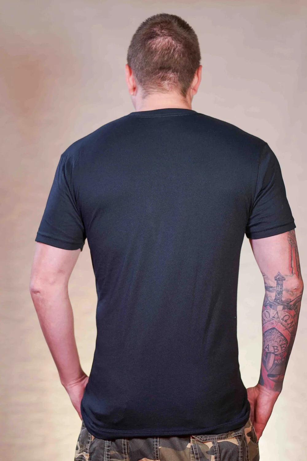 Man wearing a black t-shirt with a plain back design against a neutral background